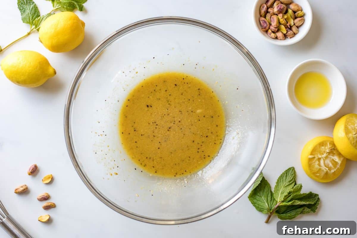 A bowl containing a freshly whisked lemon honey dressing, perfectly emulsified and ready to be combined with the blanched asparagus and peas for a delicious spring salad.