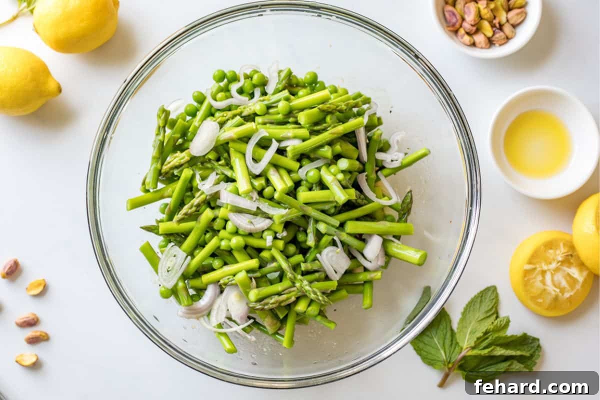 Blanched asparagus and sweet peas, mixed with thinly sliced shallots, thoroughly coated in a bright lemon dressing in a large mixing bowl, ready for chilling and serving.