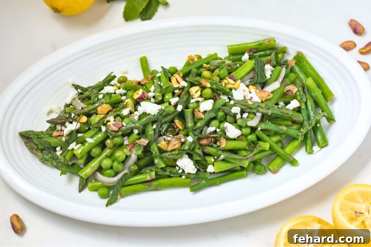 A beautifully plated asparagus and pea salad, generously garnished with crumbled feta cheese, chopped pistachios, and fresh mint, ready to be enjoyed as a refreshing spring dish.