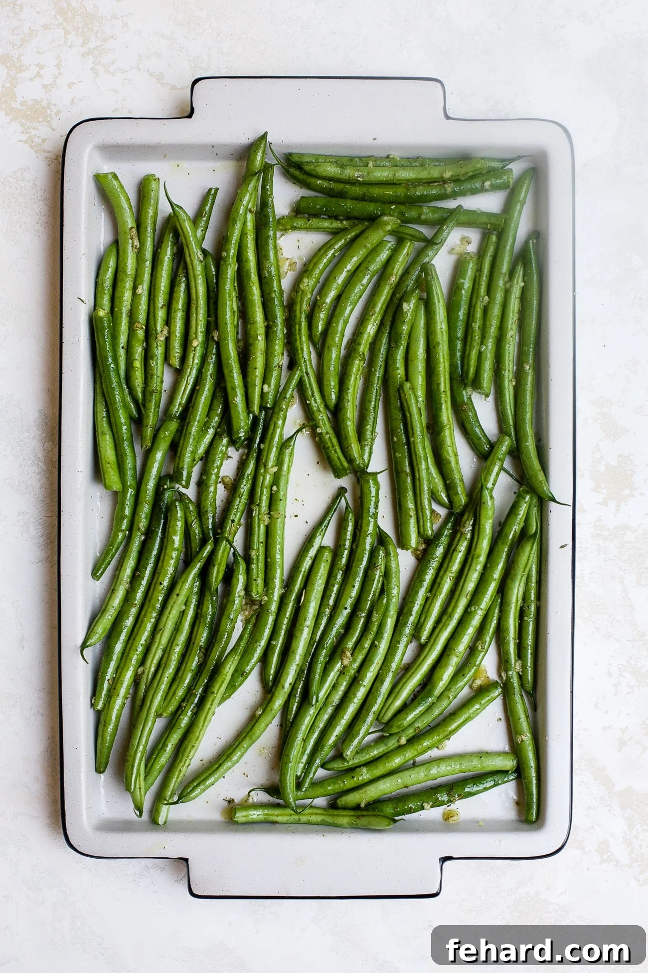 Seasoned green beans spread out in a single layer on a large baking sheet, ready for roasting.