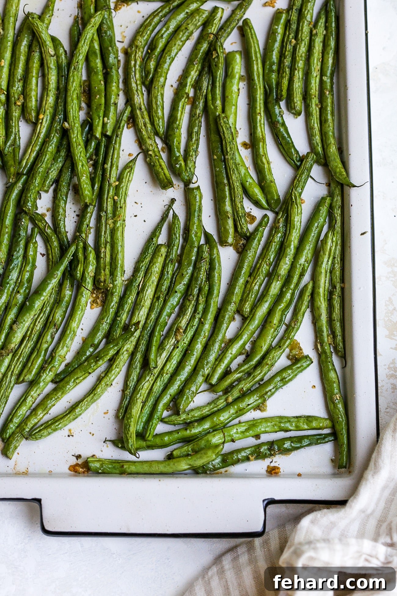 Freshly roasted green beans, golden brown and crispy, on a large baking sheet.