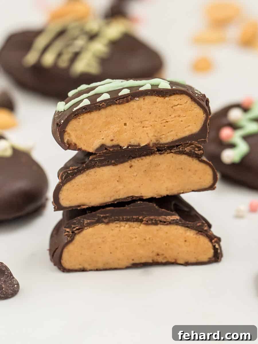 3 homemade peanut butter eggs cut open to show dark chocolate coating around creamy peanut butter filling stacked on top of eachother.