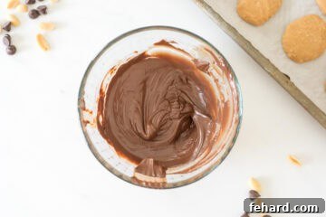 Melted dark chocolate in a narrow bowl, with chilled peanut butter eggs in the background.