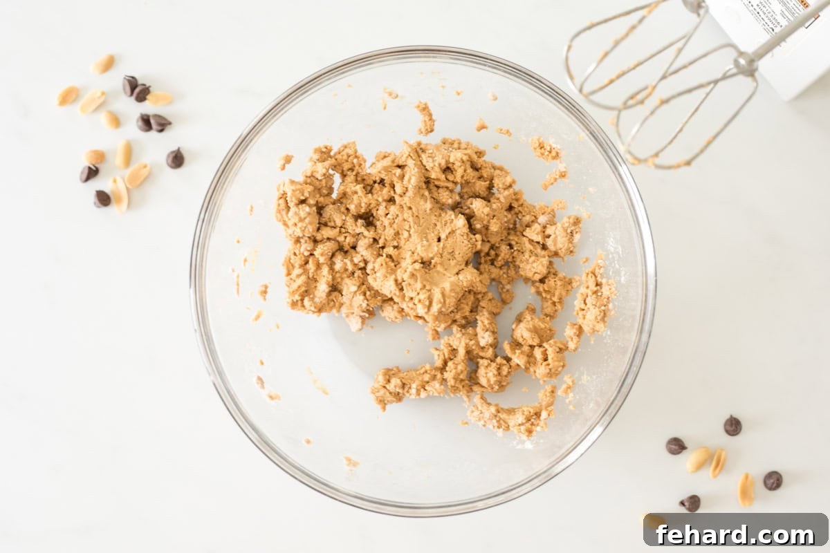 Close-up of creamy peanut butter egg filling being mixed in a large bowl, with ingredients like peanuts and chocolate chips blurred in the background, suggesting preparation.
