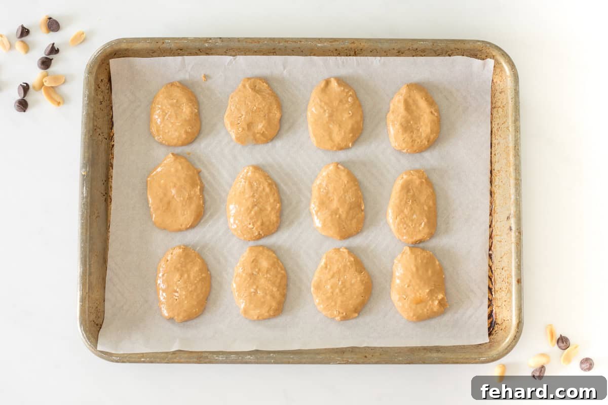 A dozen perfectly shaped raw peanut butter eggs arranged neatly on a parchment-lined baking sheet, ready for chilling and chocolate dipping.