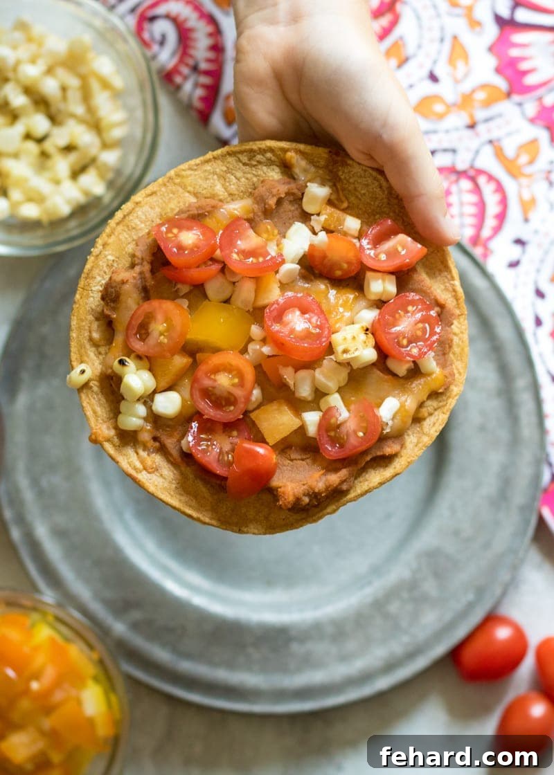 Delicious Baked Tostada with Fresh Toppings Child's hand holding a golden-brown baked tostada, generously topped with vibrant diced tomatoes and fresh corn kernels, showcasing its delicious appeal.