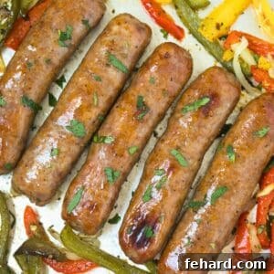 Baked Italian sausages with peppers and onions topped with minced parsley on baking sheet pan.