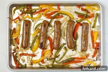 5 baked sausage links on rimmed baking sheet surrounded by onions and peppers.