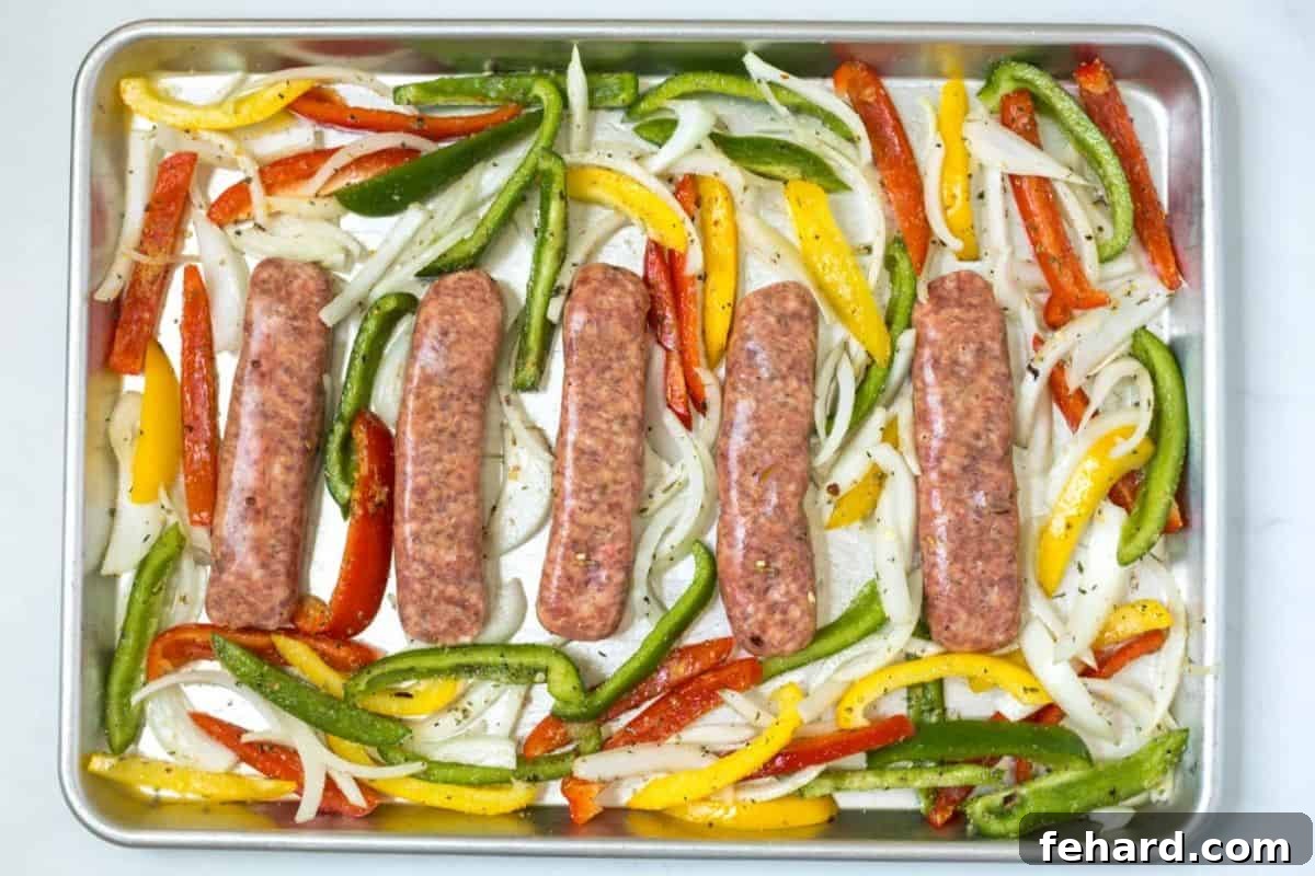 Baked Sausage with Peppers and Onions Arrangement Five raw Italian sausage links neatly arranged on a rimmed baking sheet, surrounded by seasoned slices of onions and colorful bell peppers, ready for baking.