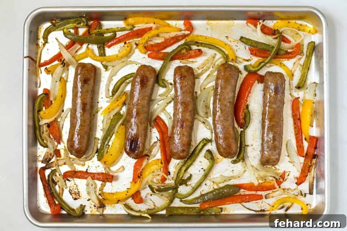 Recipe Baked Italian Sausage Cooked Five perfectly baked Italian sausage links surrounded by caramelized onions and roasted bell peppers on a rimmed baking sheet, fresh out of the oven.