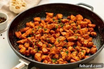 Chicken bites cooked in skillet, topped with parsley.