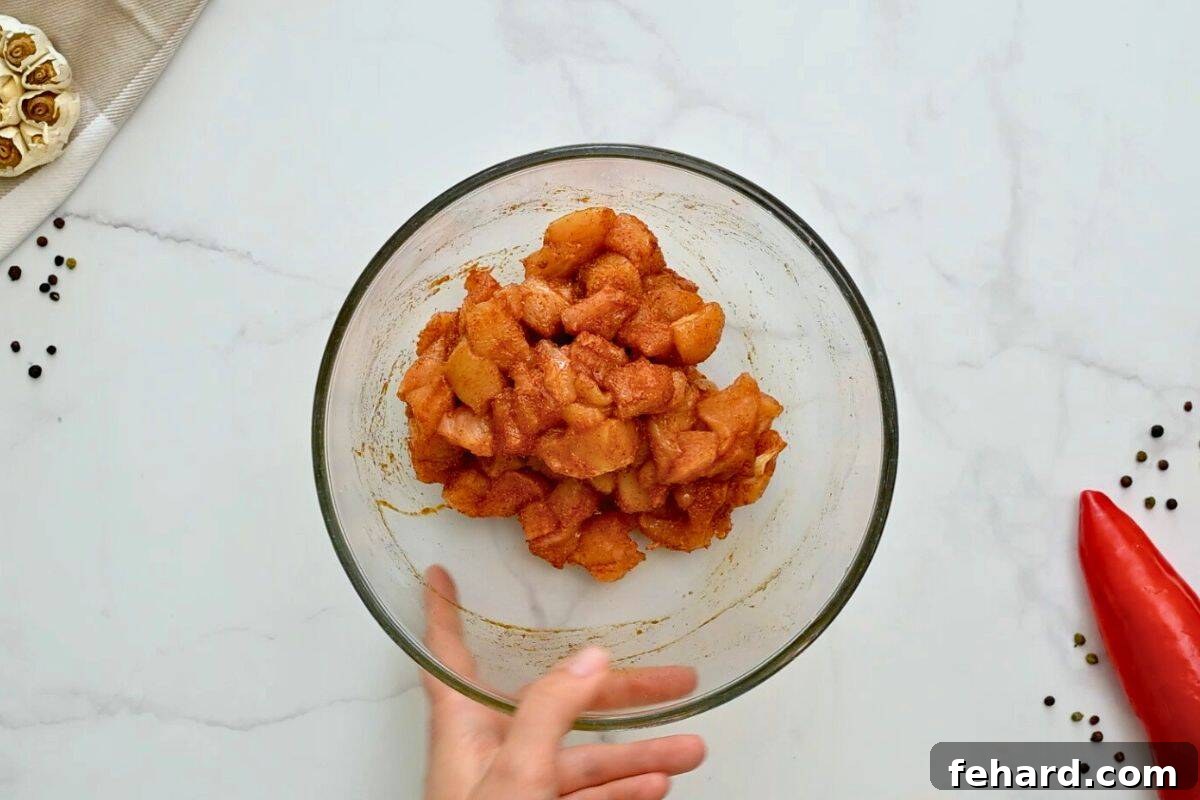 Cubed chicken breast in a large mixing bowl, thoroughly seasoned with a sweet and savory spice rub.