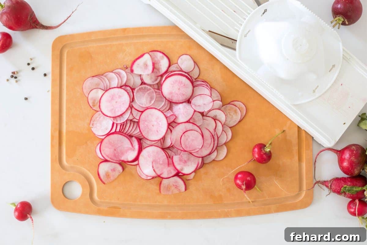 Thinly sliced red radishes neatly arranged on a wooden cutting board next to a mandoline slicer.