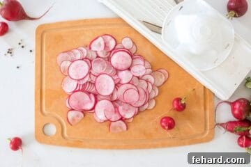 Thinly sliced red radishes on wooden cutting board next to mandoline.