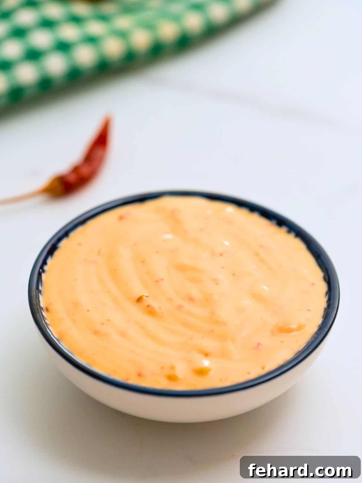 Bowl of creamy, tangy, spicy bang bang sauce with red dried chilis in background, ready to be served as a delicious dip.