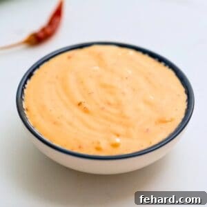 Bowl of copycat bang bang sauce with red dried chilis in background.