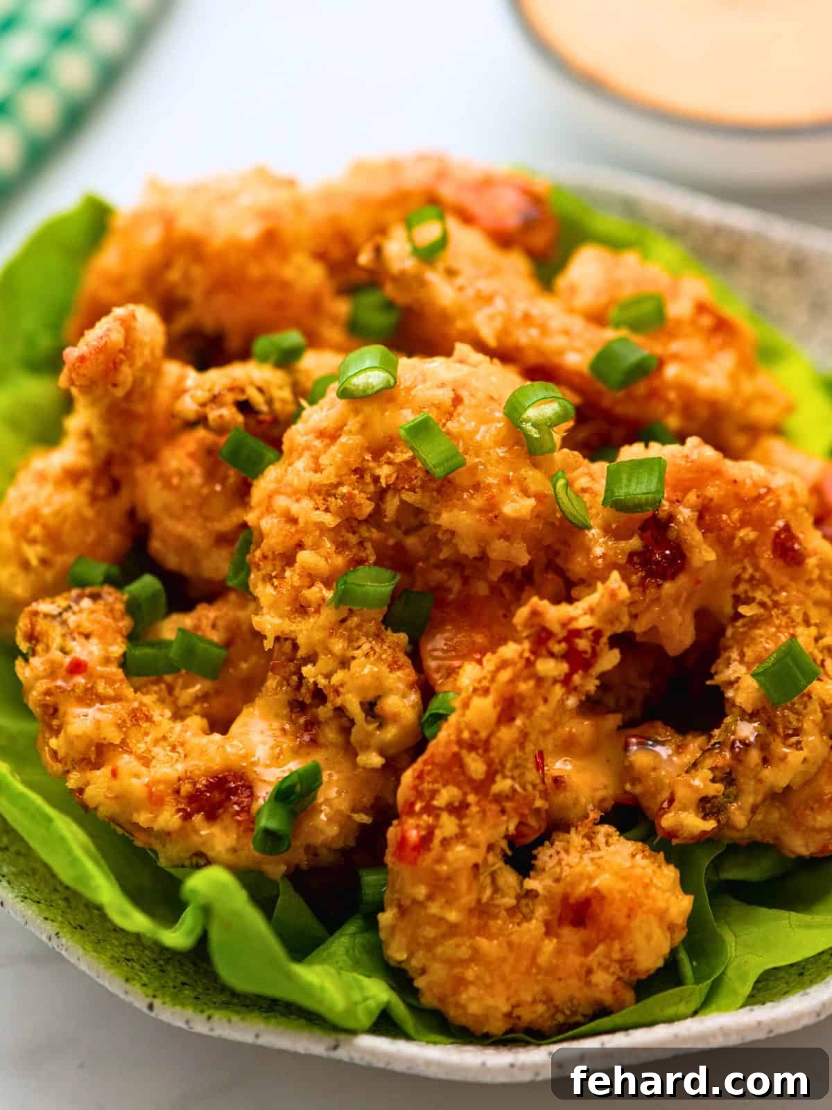 Baked Crispy Bang Bang Shrimp served beautifully on fresh bibb lettuce leaves, garnished with minced green onions, with a bowl of the signature Bang Bang sauce on the side for dipping.