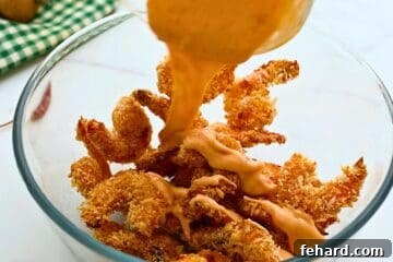 Crispy baked shrimp being gently tossed with the creamy and vibrant Bang Bang sauce in a spacious mixing bowl, ensuring every piece is coated.