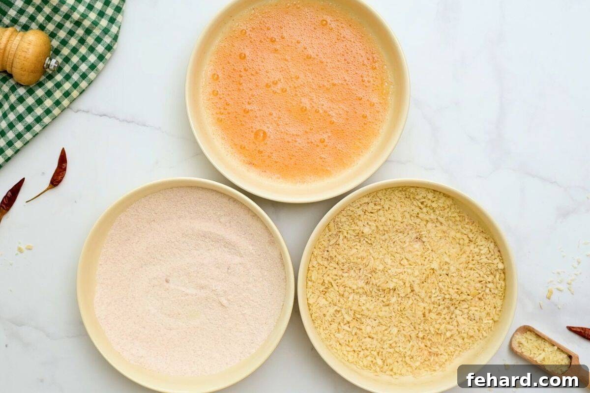 An organized breading station with three shallow dishes: one containing seasoned flour, the second holding the Sriracha-infused egg mixture, and the third filled with seasoned Panko breadcrumbs, prepared for breading shrimp.
