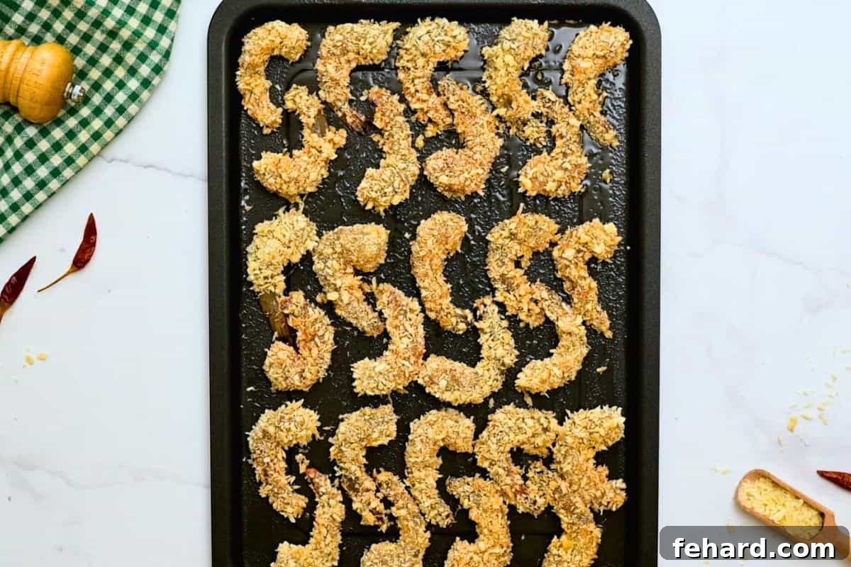 Perfectly breaded raw shrimp arranged meticulously in a single layer on a greased baking sheet, awaiting their transformation in the oven to crispy Bang Bang Shrimp.