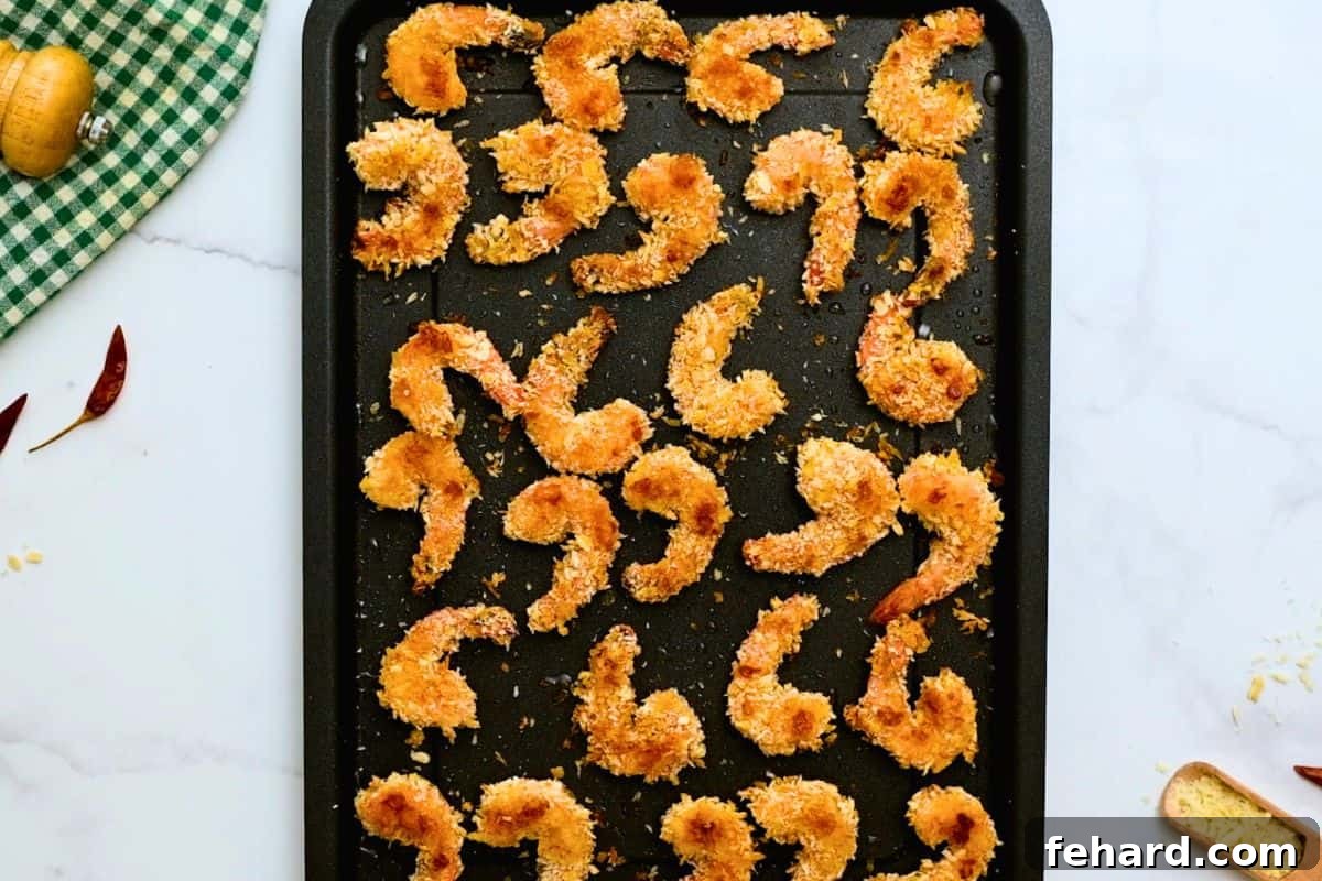 A baking sheet filled with freshly baked crispy breaded shrimp, boasting a beautiful golden-brown color and perfectly cooked texture, ready for saucing.