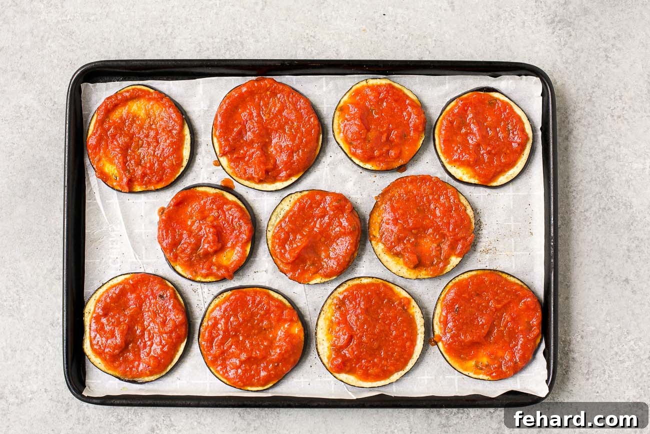 Mini Eggplant Pizzas 4 raw slices of eggplant with tomato sauce on the top on a baking sheet