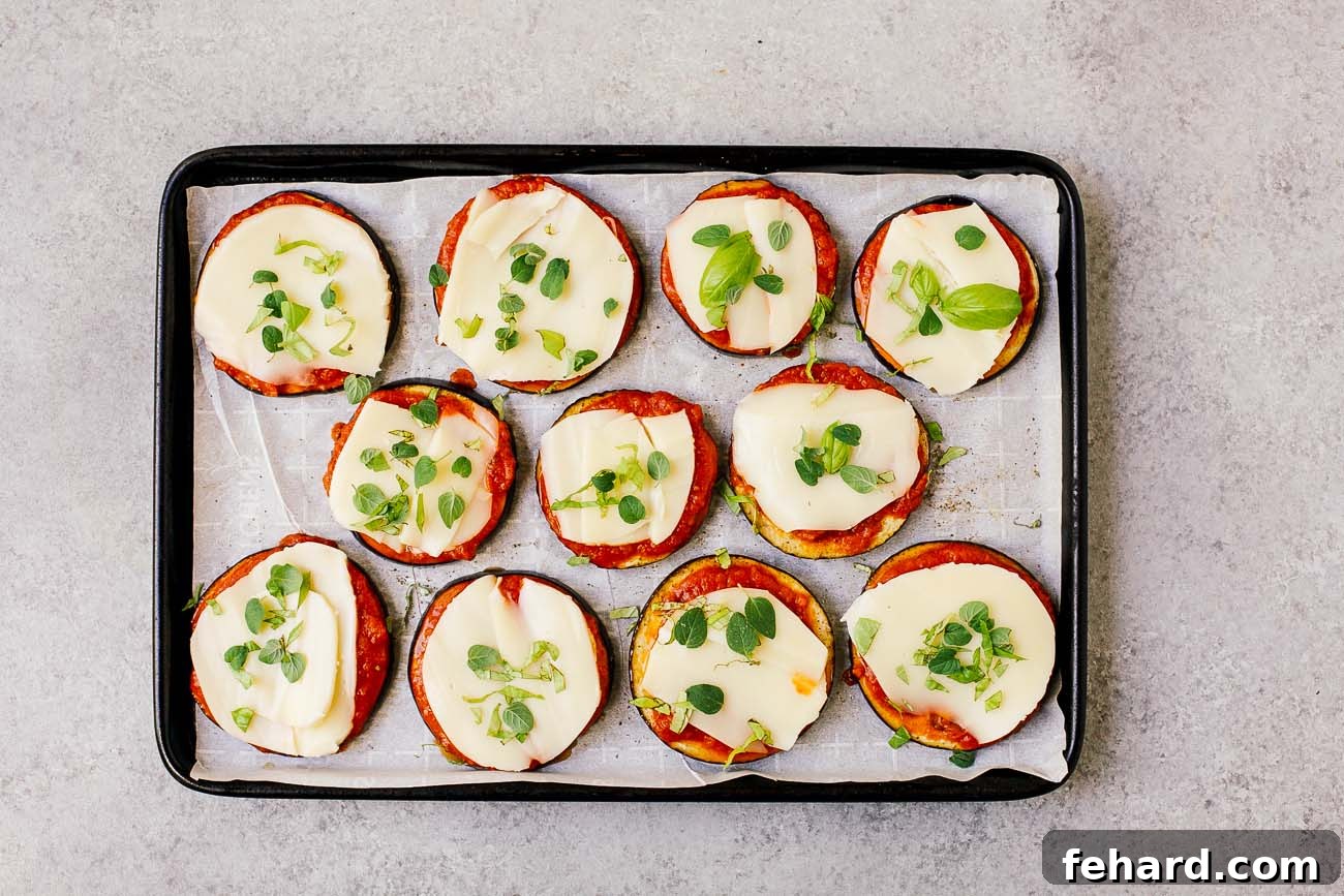 Mini Eggplant Pizzas 5 raw slices of eggplant with tomato sauce on top and mozzarella on a baking sheet