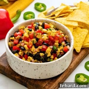 Black bean and grilled corn tossed with tomatoes, peppers, jalapenos, and lime dressing in white bowl next to tortilla chips.