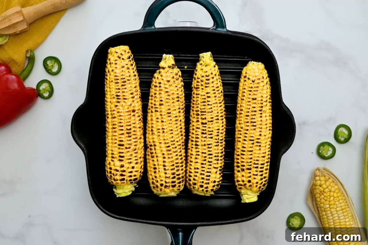 Four ears of sweet summer corn cooking on a grill plate, showing light char marks developing on the kernels.