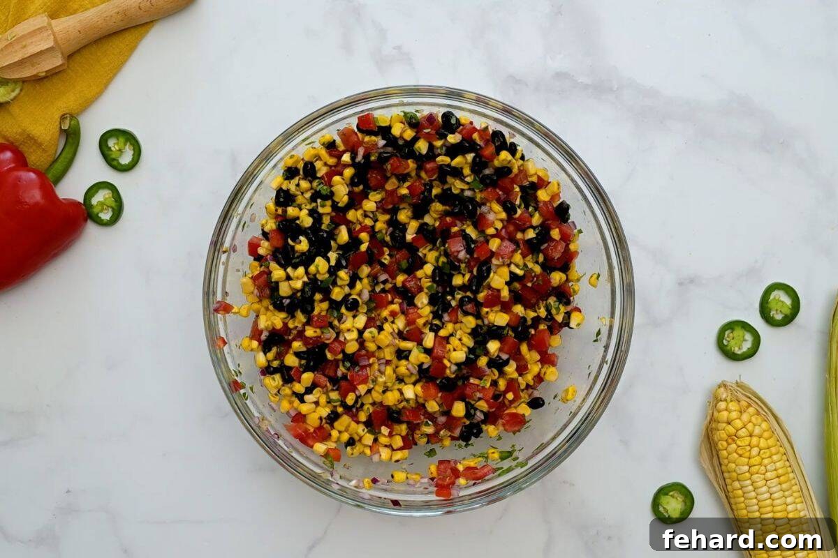 A large mixing bowl filled with vibrant black beans, grilled corn, diced tomatoes, red bell peppers, and onions, all tossed with a fresh cilantro lime dressing.