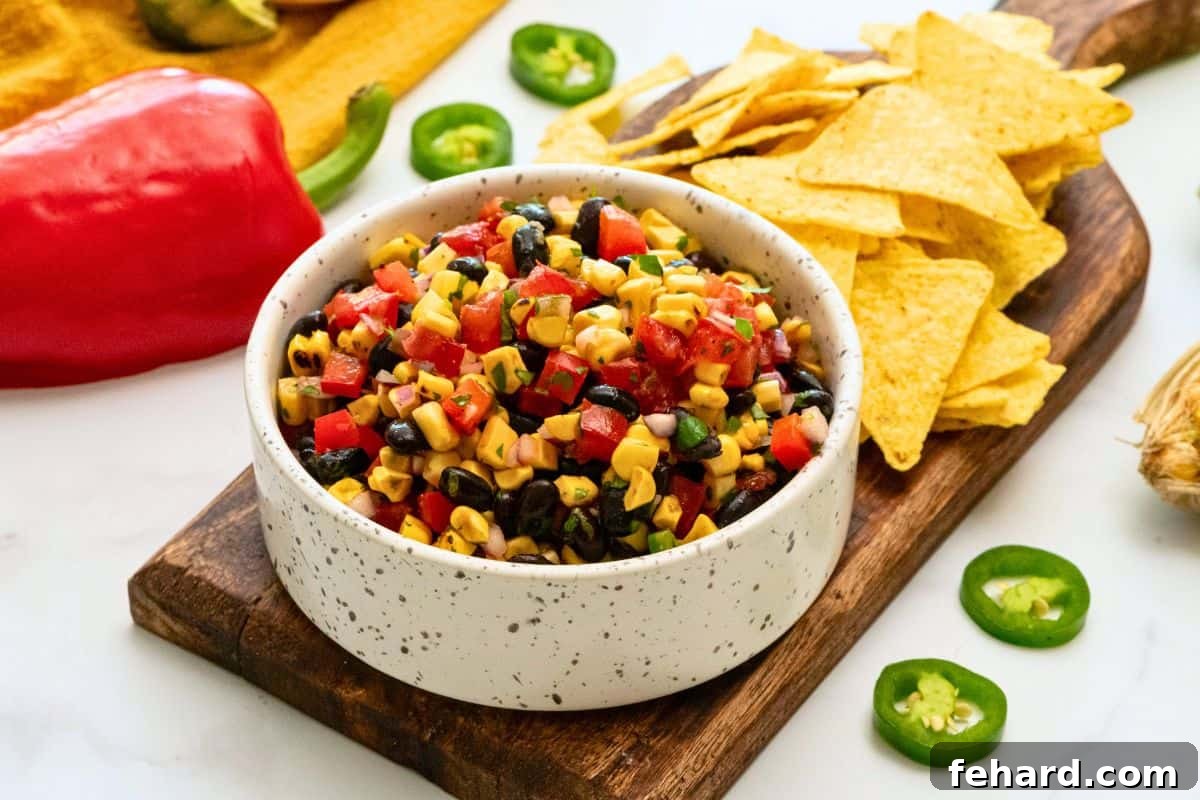 A serving bowl of homemade black bean corn salsa made with grilled corn, garnished with fresh cilantro, positioned next to a bowl of crispy tortilla chips, ready to be served.