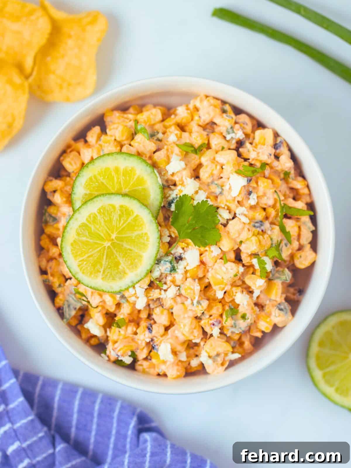 Creamy Mexican Street Corn Salad in a white bowl, garnished with sliced limes, crumbled queso fresco, and fresh cilantro leaves.