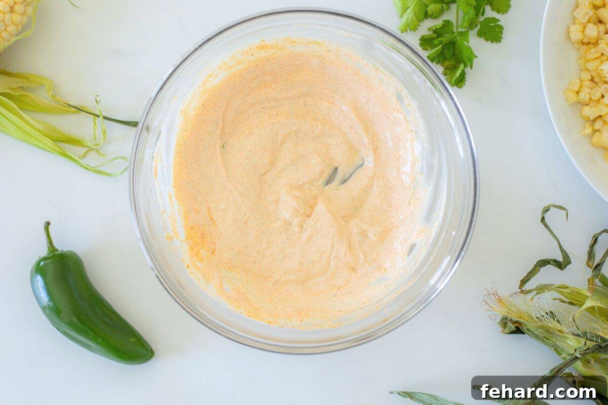A large mixing bowl containing the creamy dressing for Mexican Street Corn Salad, with fresh corn on the cob visible in the background.