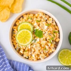 Mexican Street Corn Salad in white bowl topped with sliced limes, queso fresco, and cilantro.