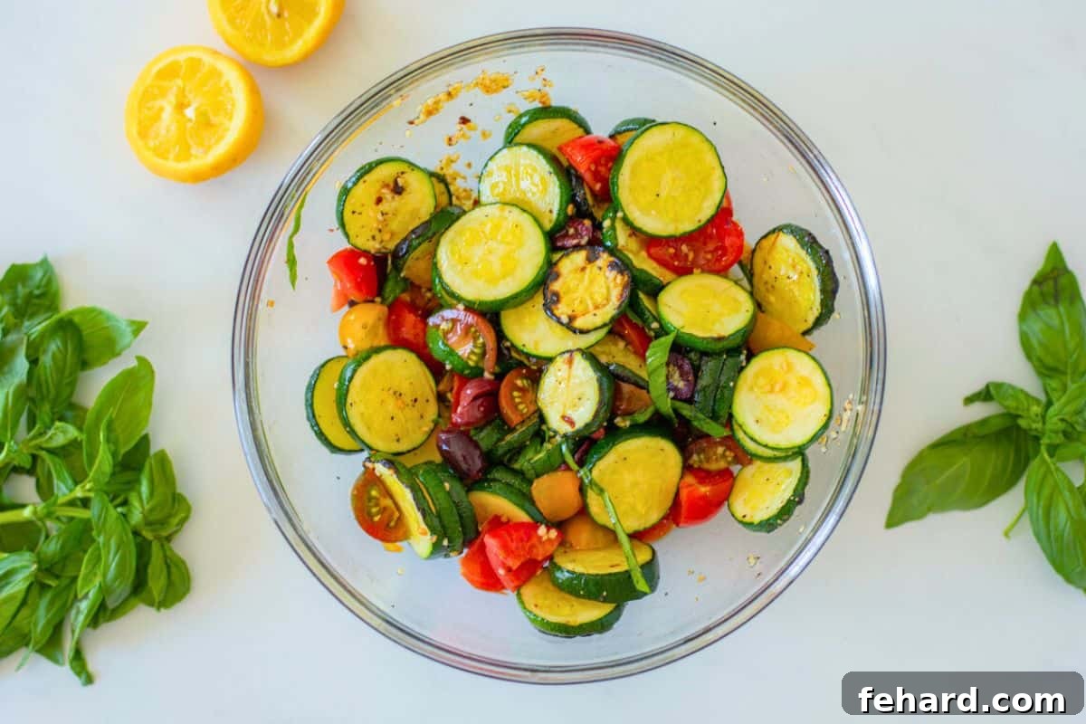 Tossing Tomato Zucchini Salad A large glass mixing bowl filled with grilled zucchini, halved cherry tomatoes, Kalamata olives, and fresh basil, all tossed with a lemon dressing, showcasing the vibrant colors and textures of the salad.