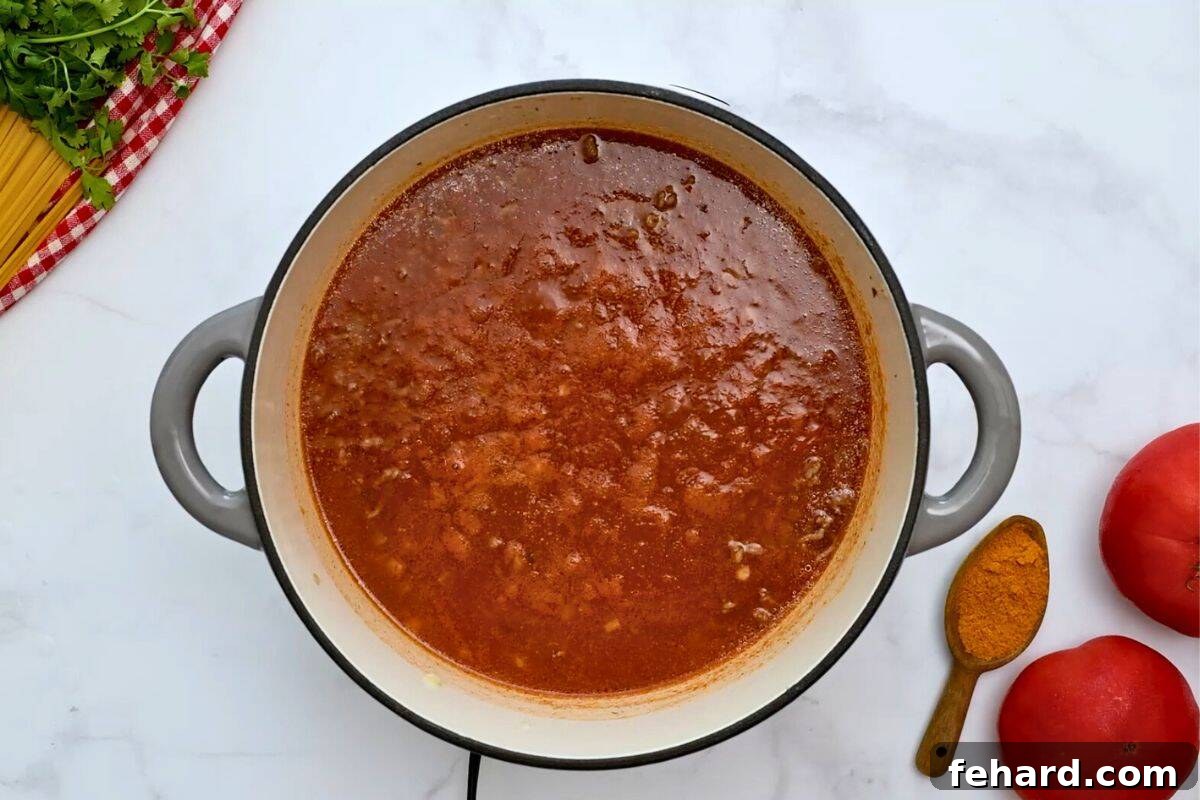 One Pot Tex Mex Spaghetti Tomato sauce, taco seasoning, and ground beef simmering in stock pan for Mexican Spaghetti.