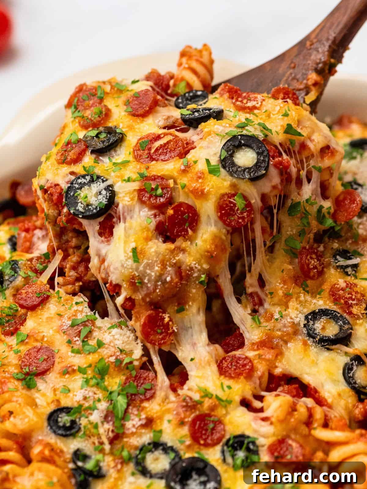 Spoonful of cheesy pasta bake with pizza sauce, pepperoni, and olives.