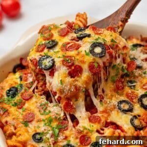 Spoonful of cheesy pizza pasta bake coming out of casserole dish topped with pepperoni and olives.
