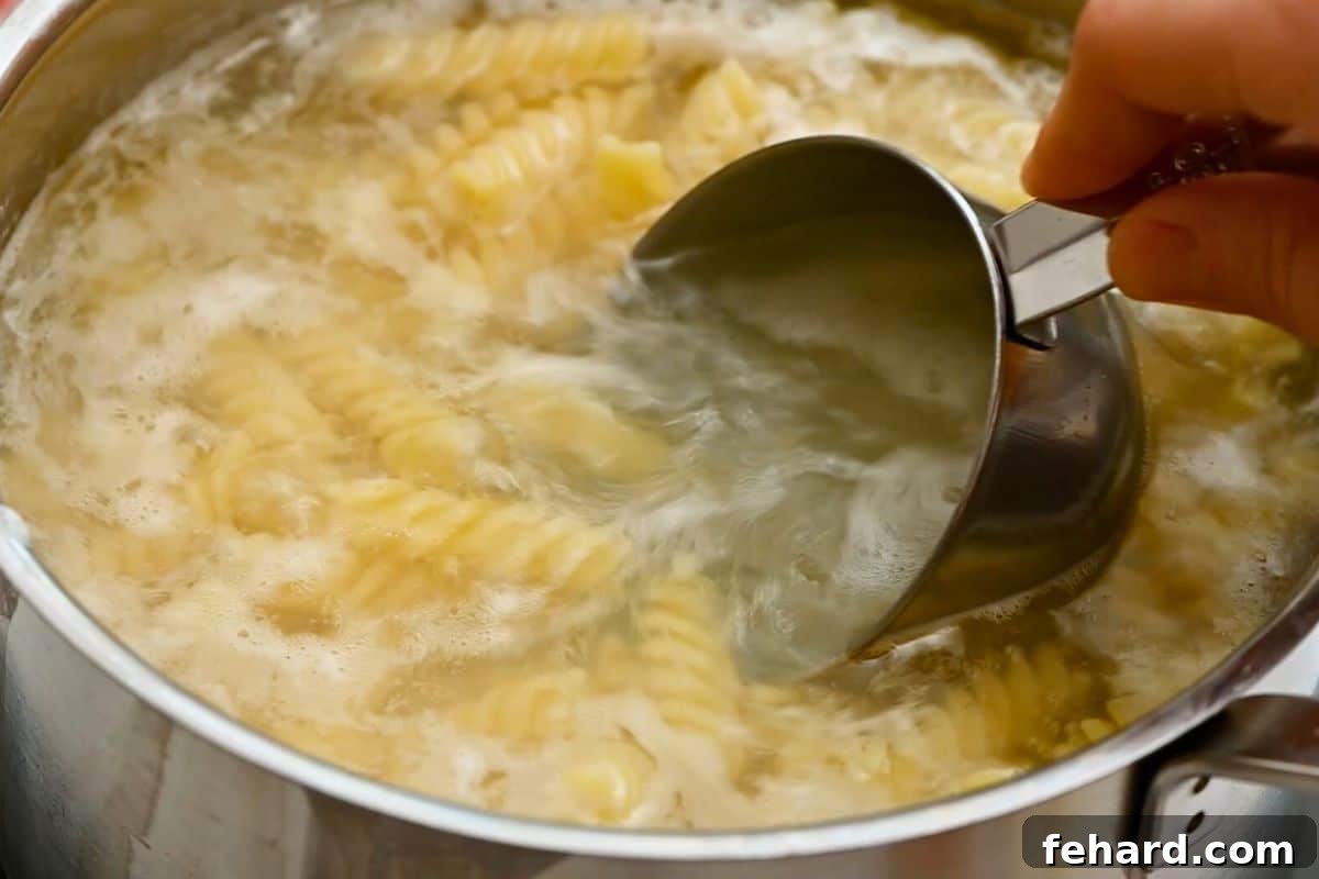 A measuring cup scooping out a bit of pasta water from boiling rotini noodles.
