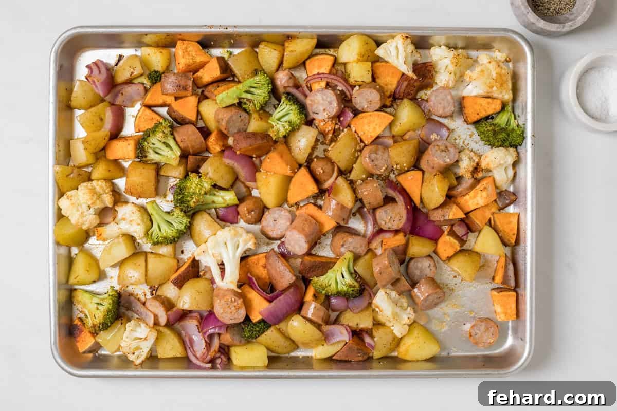 Partially roasted potatoes, sweet potatoes, broccoli, cauliflower, and red onions on rimmed sheet pan with chicken sausage slices just added and tossed.