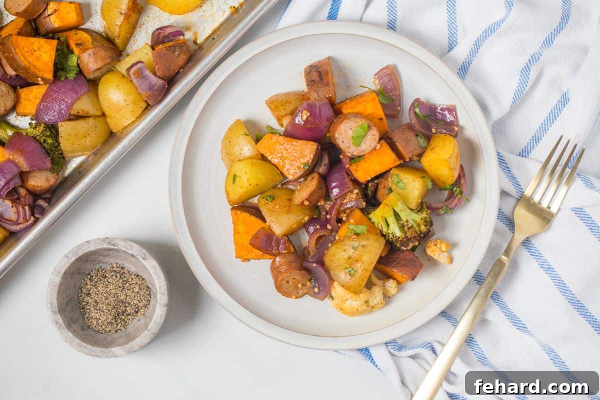 Sausage sheet pan with potatoes and veggies portioned out on a white plate, topped with fresh parsley, positioned next to the sheet pan of remaining dinner.