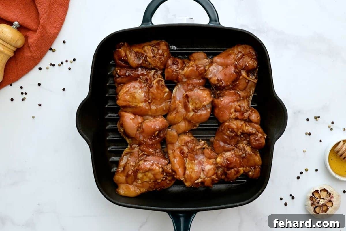 Six marinated chicken thighs placed on a hot grill plate, ready to be cooked to perfection.