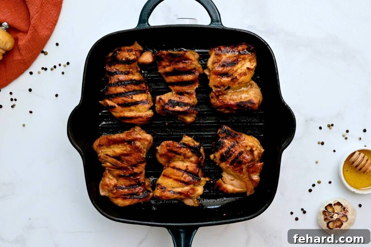Six marinated chicken thighs on a grill plate after browning on one side, showcasing a delicious sear.