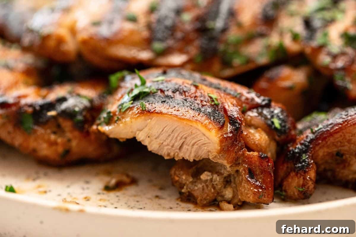 Grilled marinated chicken thighs on platter with a piece cut out to show juicy interior, ready to be served.