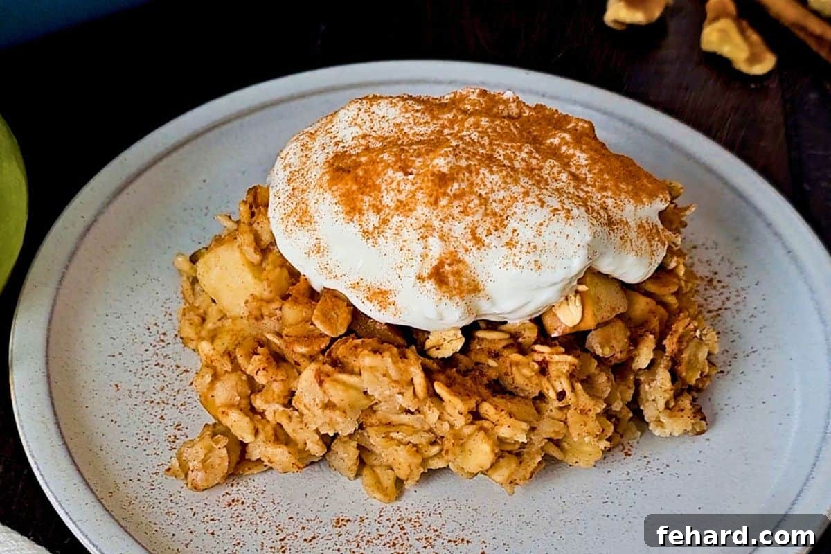 A slice of warm baked apple oatmeal on a plate, topped with a dollop of creamy Greek yogurt and a dusting of cinnamon sugar.
