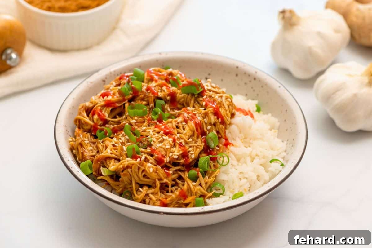 Crockpot Shredded Teriyaki Chicken served over white rice, garnished with green onions and sesame seeds.