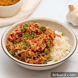 Shredded Crockpot Teriyaki Chicken served with white rice and chopped green onions in white bowl.