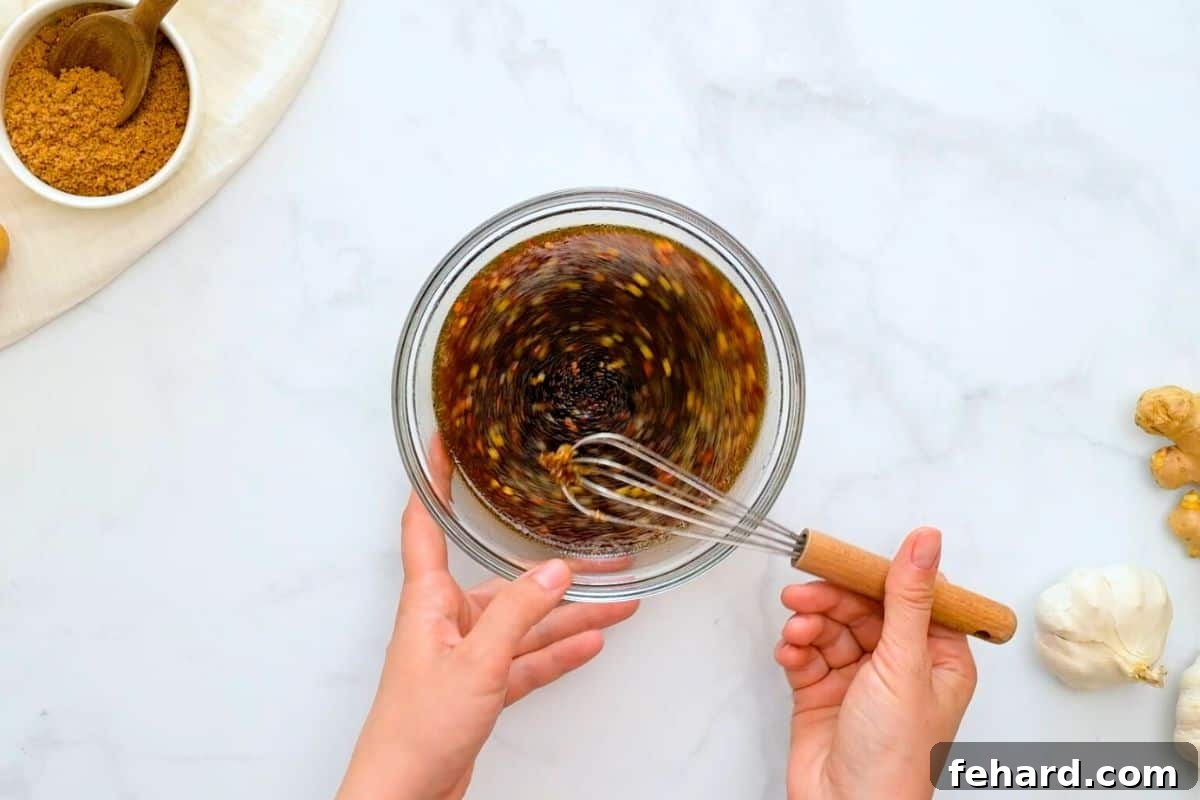 Homemade Teriyaki Sauce being whisked in a small mixing bowl next to fresh garlic and ginger.