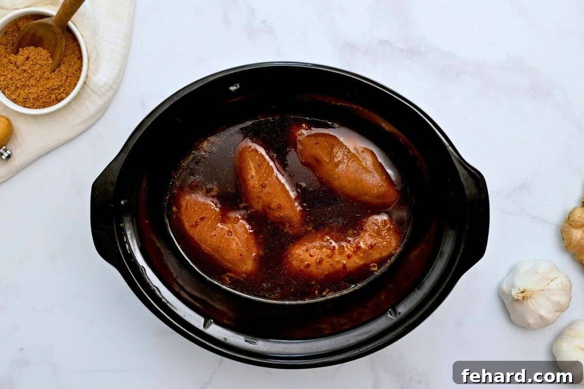 Slow cooker filled with perfectly cooked chicken breasts simmering in homemade teriyaki sauce.