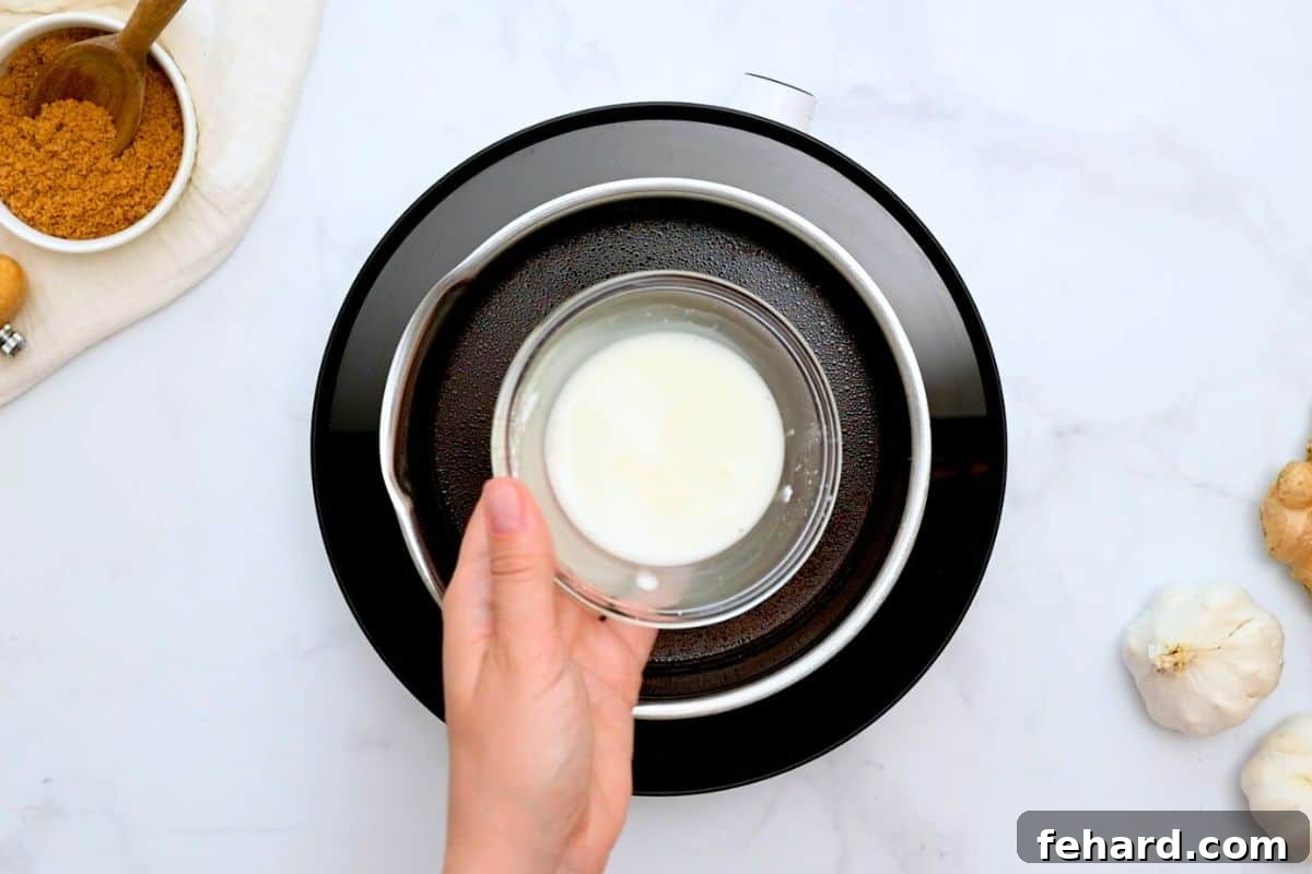 Cornstarch slurry in a small bowl being held over a pan with simmering homemade teriyaki sauce.